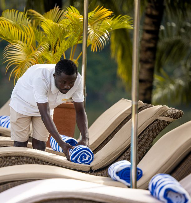 An image of a staff member placing pool towels on the beach beds surrounding the main pool at The Royal Senchi Hotel & Resort in Ghana
