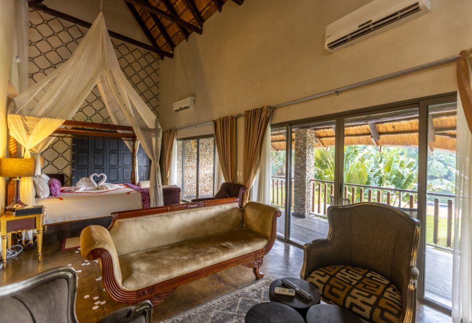 View of the four-poster bed and the lounge and views from The Picathartes Presidential Suite at The Royal Senchi Hotel & Resort, Ghana