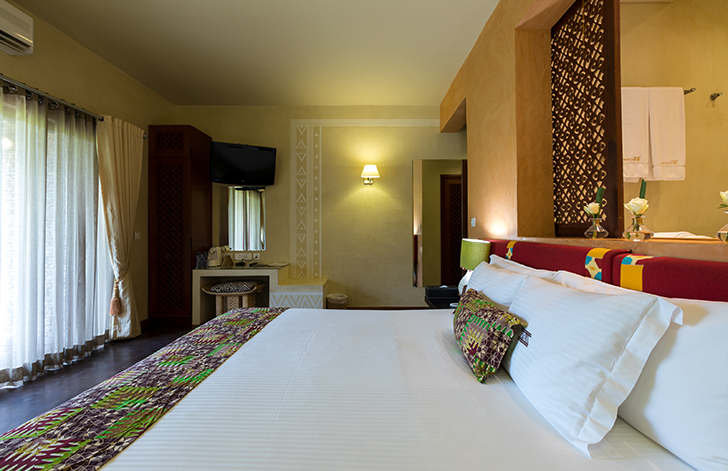 View of the bed and the view of the garden from The River View Room at The Royal Senchi Hotel & Resort, Ghana
